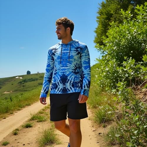 Man in blue hoodie walking on a dirt path in nature.